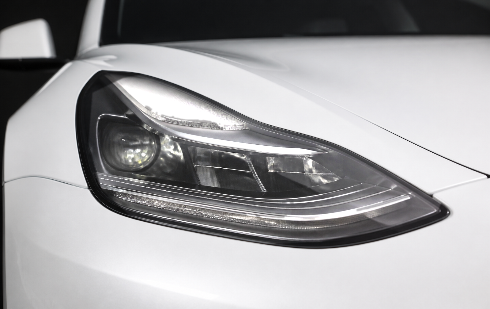 Close-up of a white Tesla Model 3 front headlight with a clear factory lens and bright internal components