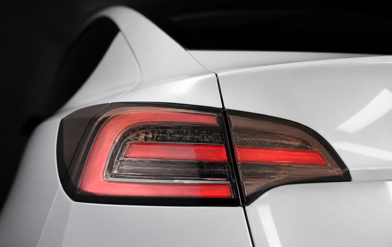 Close-up of a white Tesla Model 3 taillight with a clear factory lens and bright red lighting elements